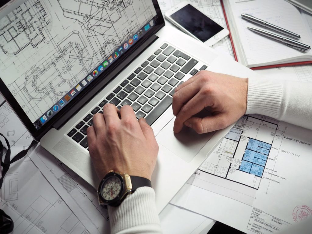 Man's hands on a laptop keyboard, blueprints underneath