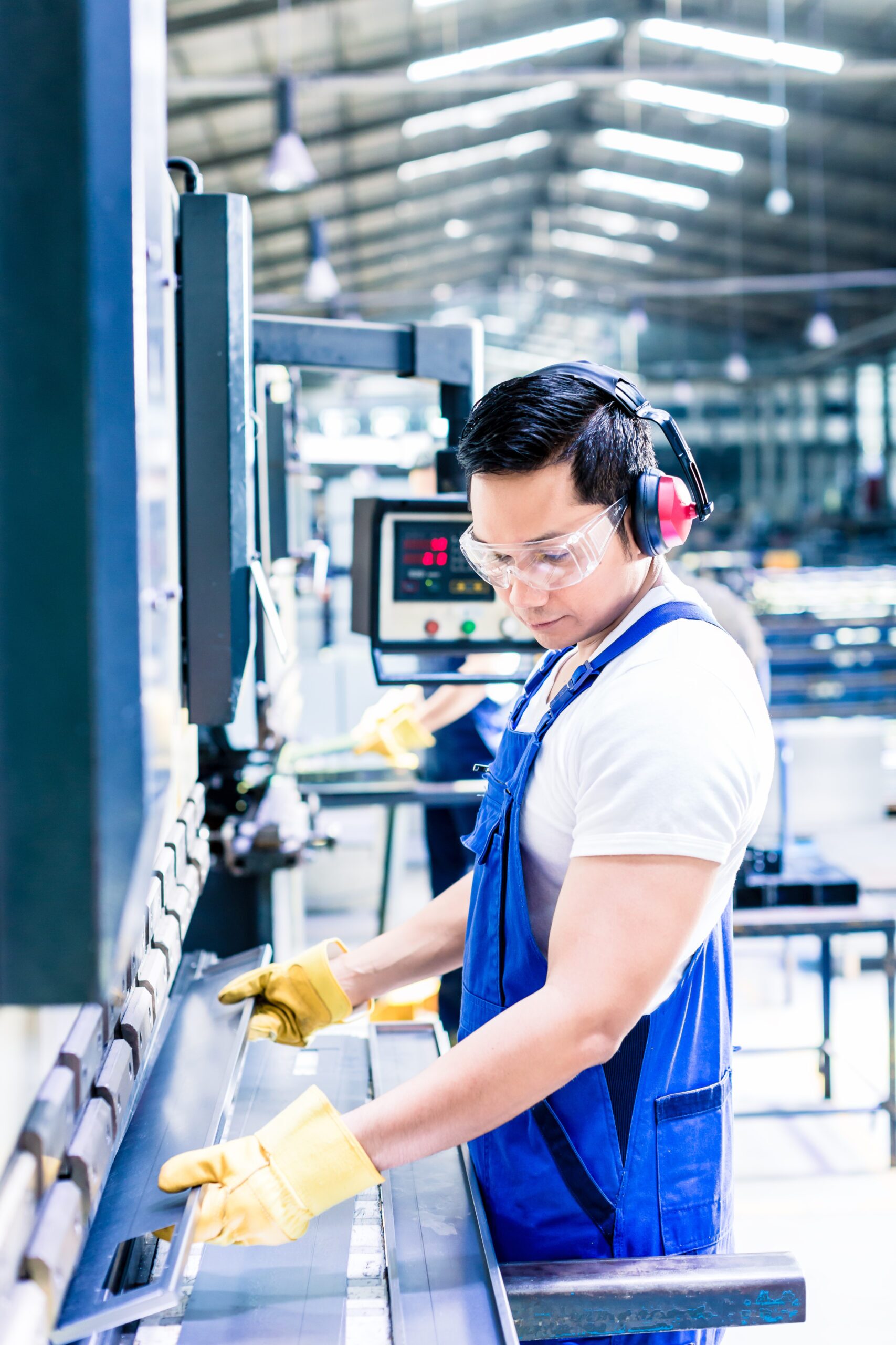 Asian worker in factory at metal skip machine putting work piece in